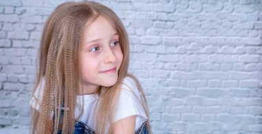 Büyük gözlü, gülümseyen bir kızın yakın portresi. Tuğla arka planı