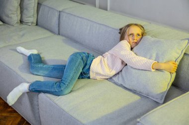 Tired little girl lying on the sofa at home clipart