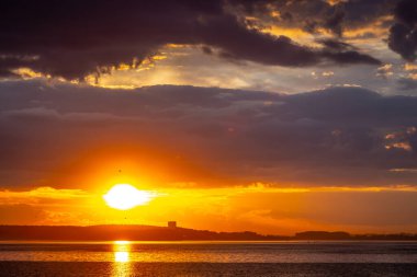 Denizin üstünde kızıl gün batımı, kara bulutlar içinde zengin.