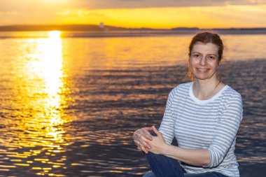 Gülümseyen kadın. Deniz kenarı ve gün batımı görünümü arkaplanı.