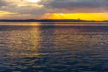 Denizin üstünde kızıl gün batımı, kara bulutlar içinde zengin.