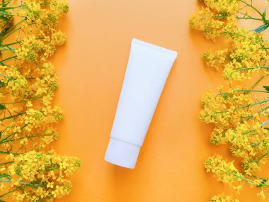 Beyaz sıkılmış şişe kozmetik tüpü ve sarı desenli arka planda sarı kır çiçekleri. Moda gölge, üst görüş, kopyalama alanı. Lüks düz konum