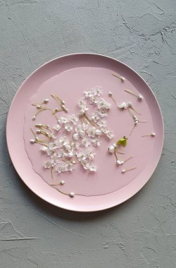 Su ve küçük alyum çiçekleri pembe bir tabakta. Yaşam tarzı, çiçekçi kahvaltı konsepti, gri arka plan. Üst görünüm