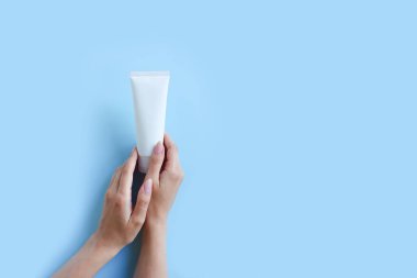 Beyaz sıkılmış şişe kozmetik tüpü ve mavi arka planda kadın eli. Üst Manzara. Doğal organik spa kozmetik konsepti. Flatlay, boşluğu kopyala