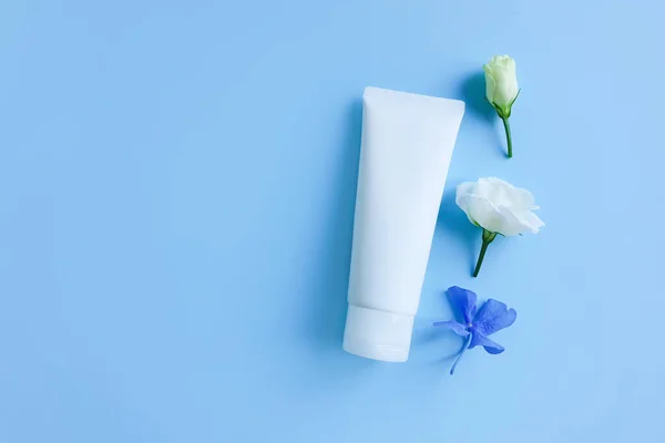 Damgasız beyaz sıkılmış şişe tüpü ve mavi masanın üzerinde küçük çiçekler. Üst Manzara. Doğal organik spa kozmetik konsepti. Damgalama ve etiketleme için boşluk.