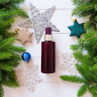 Koyu kahverengi sprey sprey maketi, köknar dalları, yıldızlar, beyaz ahşap masadaki toplar. Damgalamak için boş etiket şişesi. Doğal organik spa kozmetik konsepti. Yakın plan, Noel düzlüğü.
