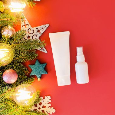 Kırmızı masada markalaştırma, etiketleme ve noel dekorasyonu için iki markasız beyaz şişe. Bunlardan biri sıkılmış plastik tüp. Diğeri plastik sprey şişesi..
