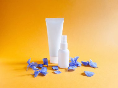 Kalıplı parlak turuncu arka planda damgalamak ve etiketlemek için iki markasız beyaz şişenin maketleri. Bunlardan biri sıkılmış plastik tüp. Diğeri plastik sprey şişesi. Doğal organik spa