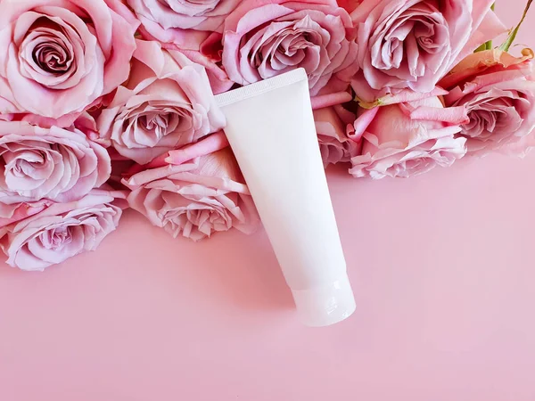 Mock-up of white squeeze bottle plastic tube and pink roses on a pastel pink background. Bottle for branding and label. Natural organic spa cosmetic. Copy space, Flower flatlay, top view.