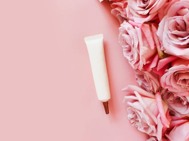 Uzun başlıklı, bronz vida kapaklı ve pembe masadaki güllerle sıkılmış kozmetik tüpün maketi. Damgalamak için bir şişe. Üst manzara, düz yatış. Boşluğu kopyala.