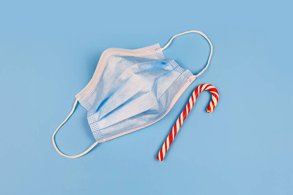 Голубая защитная медицинская маска и мятный леденец в полоску на синем фоне. Крупный план.
