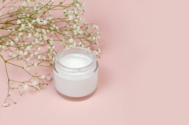 Açık cam kavanozda nemlendirici krem ve pembe arka planda çingene çiçeği. Doğal organik spa kozmetik konsepti. Ön görünüm ve boşluk kopyala