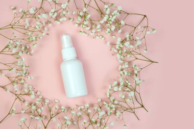 Beyaz plastik sprey şişesi ve pembe arka planda çingene çiçekleri. Doğal organik kaplıca ürünleri ve sıvı antimikrobik sprey konsepti..