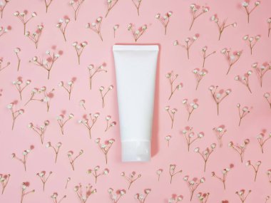 İlaç veya kozmetik ürünlerini damgalamak için beyaz sıkılmış plastik şişe tüpü. Krem, jöle, cilt bakımı. Kozmetik şişe kabı ve pembe arka planda çingene çiçekleri..