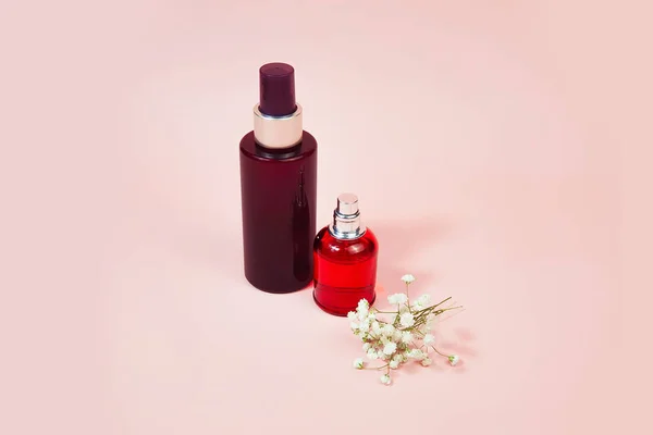 Perfume spray red bottle, brown plastic spray bottle and gypsophila flowers on pink background with copy space. Front view, mockup. Bottles for branding and label.