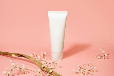 Beyaz plastik tüp ve açık pembe arka planda çingene çiçeklerinin üst görüntüsü. Doğal organik spa kozmetik konsepti. Ön görünüm