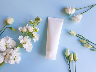 İlaç ya da kozmetik ürünleri markalaştırmak için kullanılan beyaz sıkılmış plastik tüplerin üst görüntüsü. Krem, jöle, cilt bakımı. Kozmetik şişe kabı ve beyaz çiçekler mavi arka plan.