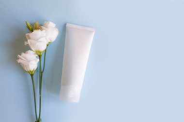 Mavi arka planda beyaz sıkma şişe kozmetik tüpü ve Eustoma çiçeği modeli, üst görünüm, kopyalama alanı.