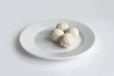 Tatlı toplar, beyaz çikolata şekerleri, beyaz arka planda hindistan cevizi kırıntısı ve beyaz tabak. El yapımı şekerler. Ön görünüm, model.