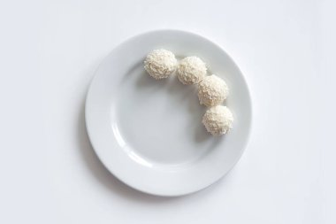 Tatlı toplar, beyaz çikolata şekerleri ve beyaz tabakta hindistan cevizi kırıntıları. Boşluğu kopyala, üst görünüm, maket.