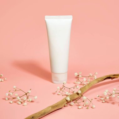 Beyaz plastik tüp ve açık pembe arka planda çingene çiçeklerinin üst görüntüsü. Doğal organik spa kozmetik konsepti. Ön görünüm