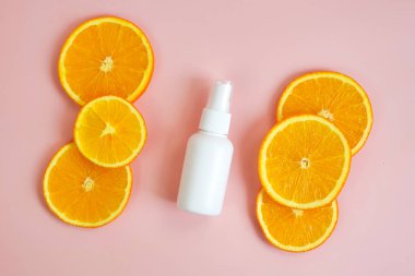 C vitamini markalaştırma konseptli sıvı antibakteriyel sprey. Üstte yukarıda düz açılı fotoğraf sprey şişesi, gerekli losyon C vitamini ve pembe arka planda turuncu dilimler var.