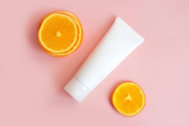 C vitamini markalaştırma konsepti ve pembe arka planda portakal dilimleri olan krema tüpü. Kozmetik cilt ürünleri boş plastik paket. Beyaz markasız losyon, balsam, el kremi, diş macunu modeli..