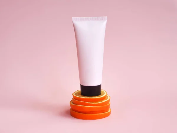 Mockup of pink squeeze bottle plastic tube with black cap on orange slices stand on pink background. Bottle for branding and label. Eco-friendly, organic cosmetology concept. Front view