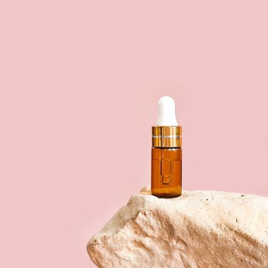 Yüz bakımı için kozmetoloji ürünü. Serum cam şişede, pipeti taşın üstünde. Kadın derisi için gerekli yağ. Cilt bakımı, pembe arka planda nemlendirici güzellik ürünü.