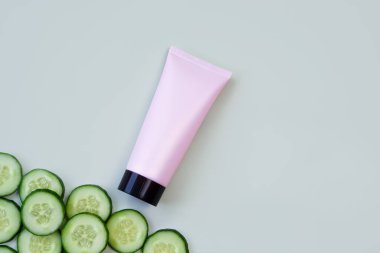 Siyah vida kapağı ve açık yeşil arka planda salatalık dilimleri ile markasız pembe sıkılmış kozmetik tüp. Cilt bakımı ve reklam konsepti. Model biçimi ve kopyalama alanı.