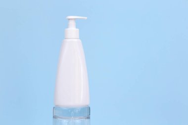 Markasız beyaz pompa kremi ya da cam podyumda mavi arka planda sıvı sabun şişesi. Kopya alanı ile kozmetik ambalajlama. Şablon, ön görünüm.