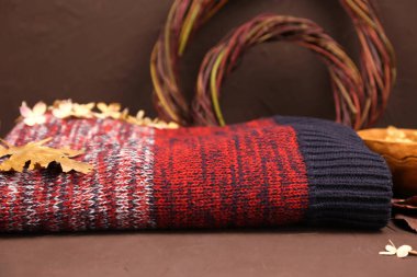 Katlanmış kırmızı örgü süveter, sonbahar yaprakları, kahverengi arka planda deren çelenk. Kozmetik ürünleri reklam arkaplanı, maket. Sıcak atmosfer.