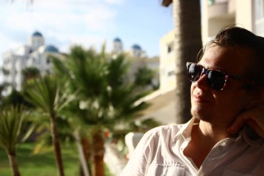 Palmiye ağaçlarında güneş gözlüğü ve güzel bir geçmişi olan beyaz bir genç. Seçici odak