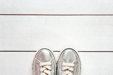 Beyaz ahşap arka planda çocuk metalik gümüş ayakkabılar fotokopi alanı ile birlikte. Kızlar için beyaz spor ayakkabılar. Üst görünüm