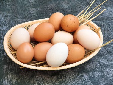 White and red brown eggs of domestic hens in basket on old wooden texture background. Front view, close-up.