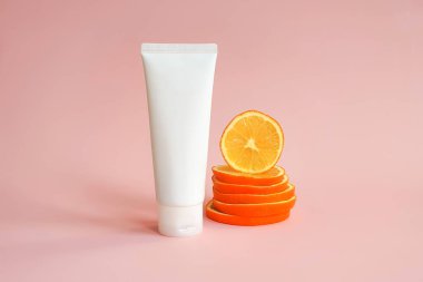 White squeeze bottle plastic tube for branding of medicine or cosmetics - cream, gel, skin care. Cosmetic bottle container and stack of orange slices on pink background. Mockup. Skincare and beauty.