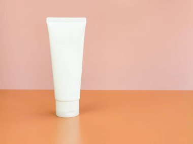 İlaç ya da kozmetik ürünleri markalaştırmak için kullanılan beyaz sıkılmış plastik tüplerin ön görüntüsü - krem, jöle, cilt bakımı, diş macunu. Şeftali ve pembe arka planda kozmetik şişe kabı.