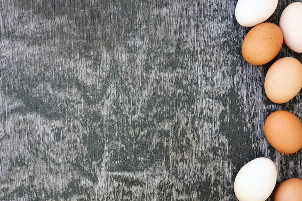 White and brown eggs of domestic hens on old wooden gray painted texture background. Top view, copy space, border or frame