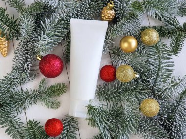 Beyaz ahşap zemin üzerinde beyaz kozmetik sıkma tüpü ve karlı Noel ağacı dalları ve kırmızı altın toplar. Model, şablon. Vücut losyonu için konteyner, krem.