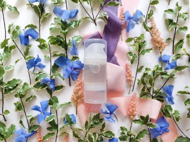 Şeffaf kayganlaştırıcı jel, taze yeşiller, mavi ve pembe çiçekler, beyaz arka planda ipek kurdeleler. Samimi masaj ve konforlu seks kutsaması. Üst görünüm, model, şablon.