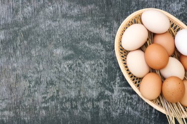Beyaz ve kahverengi evcil tavukların yumurtaları eski ahşap gri doku arka planında örülmüş saman sepetinde. Üst görünüm, alanı kopyala