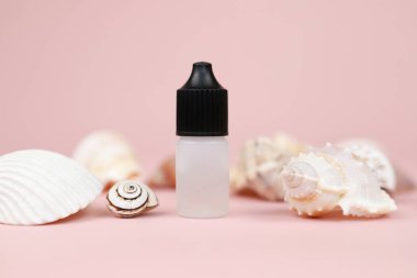 Bir şişe alet yağı, budama yağı ve pembe arka planda bir sürü farklı deniz kabuğu. Mockup, ön görünüm.