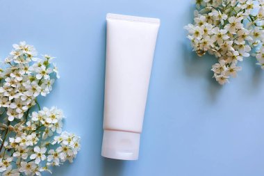 Markasız beyaz kozmetik sıkma tüpü ve mavi arka planda beyaz kuş kirazı çiçekleri. Model, şablon. Vücut losyonu için konteyner, nemlendirici krem, duş jeli, tıraş kremi..