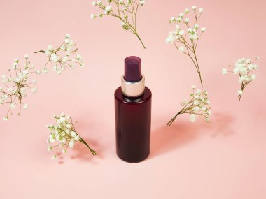 Markasız kahverengi kozmetik sprey şişesi ve pembe arka planda uçan çigila çiçekleri. Doğal organik kaplıca ürünleri. Vücut sisi, Mockup, şablon.