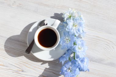 Kahve fincanı çay tabağı ve kaşık, mavi Delphinium çiçeği beyaz ahşap masa üzerinde ve son moda gölge. Üst Manzara, düz çizgi. Metnin ve ürünün için yer aç. Aroma ve günaydın konsepti.
