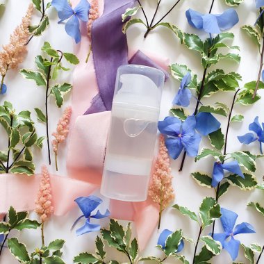 Şeffaf kayganlaştırıcı jel, taze yeşiller, mavi ve pembe çiçekler, beyaz arka planda ipek kurdeleler. Samimi masaj ve konforlu seks kutsaması. Ön görünüm, model, şablon.