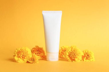 İlaç ya da kozmetik ürünleri markalaştırmak için kullanılan beyaz sıkma şişe kozmetik krem tüpü. Şampuan, jöle, cilt bakımı. Nemlendirici boş şişe ve sarı arka planda kadife çiçekleri. Ön görünüm.