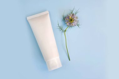 Beyaz sıkılmış şişe kozmetik krem tüpü ve mavi arka planda mavi Nigella çiçeği. Üst görünüm, maket, fotokopi alanı olan düz stil. Cilt bakımı. Modelleme. Kozmetik spa şişesi boş.