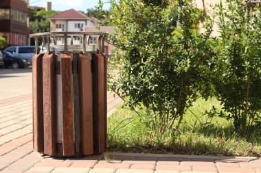 Kahverengi ahşap çöp tenekesi ve bulanık arka planı olan sokaktaki çalılık..