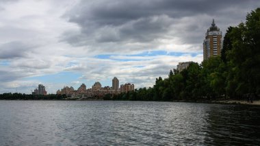 sakin nehir manzarası ve bulutlu gökyüzü arka planındaki ağaçların arkasındaki binalar, doğa kavramı, Kyiv, Ukrayna